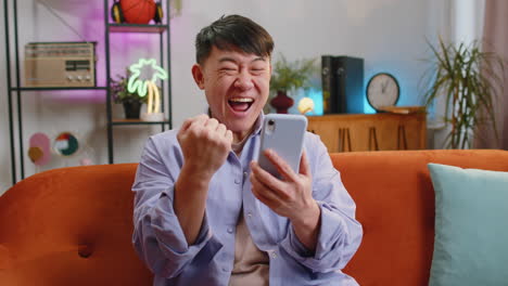 Happy-asian-man-at-home-use-smartphone-typing-browsing-wow-yes-found-out-great-big-win-celebrate