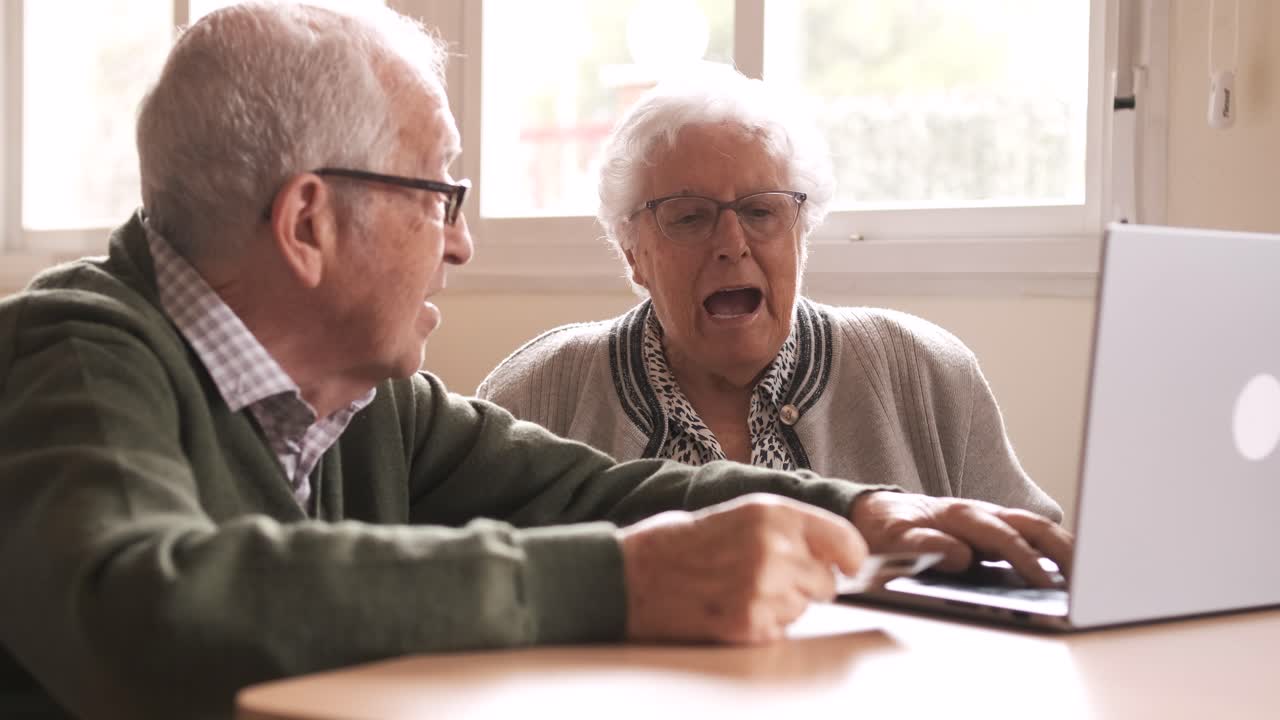 Happy elderly man and woman using laptop and credit card at nursing home
