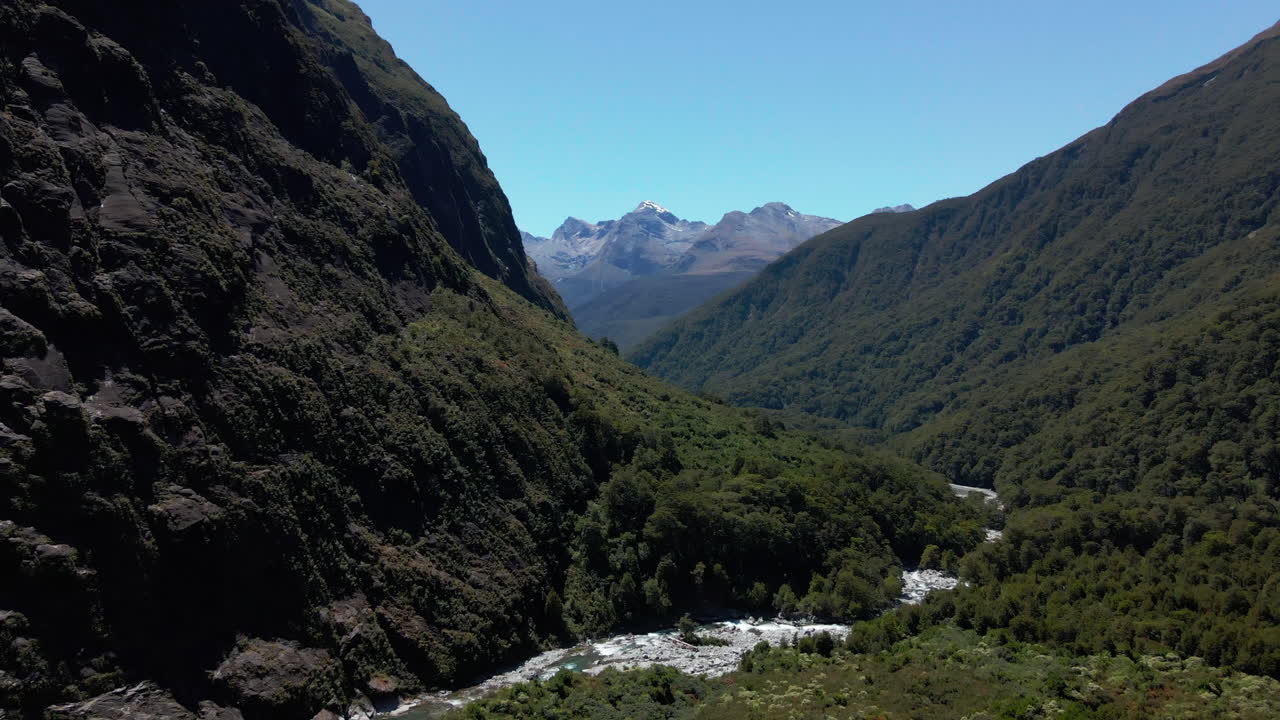 río de montaña salvaje que se abre paso a través de un estrecho valle debajo de los picos de las montañas en fiordland southland, nueva zelanda