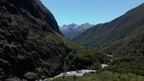 río de montaña salvaje que se abre paso a través de un estrecho valle debajo de los picos de las montañas en fiordland southland, nueva zelanda