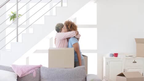 Happy-diverse-female-lesbian-couple-with-boxes-moving-house-and-embracing-in-slow-motion