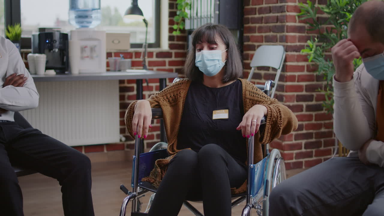 Sad woman sitting in wheelchair and crying at aa rehab meeting with group of people