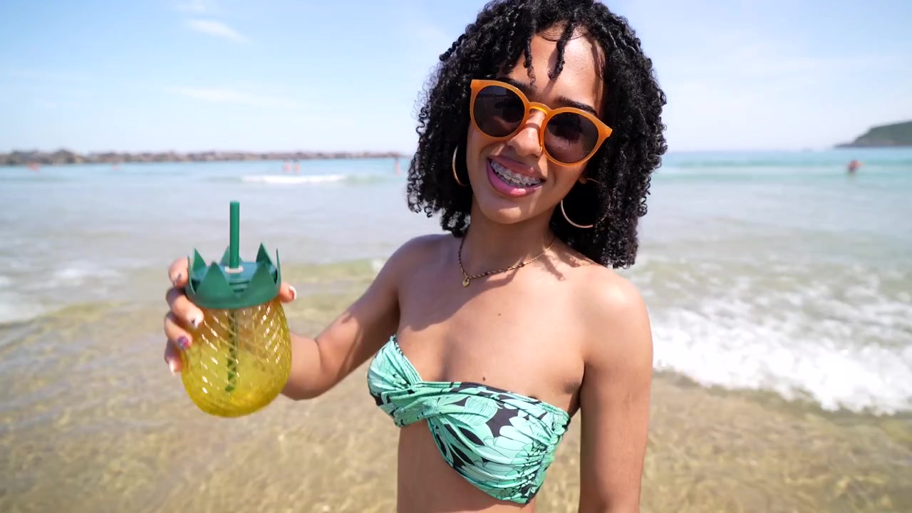 Jovem mulher feliz sorrindo e segurando uma bebida de abacaxi na praia