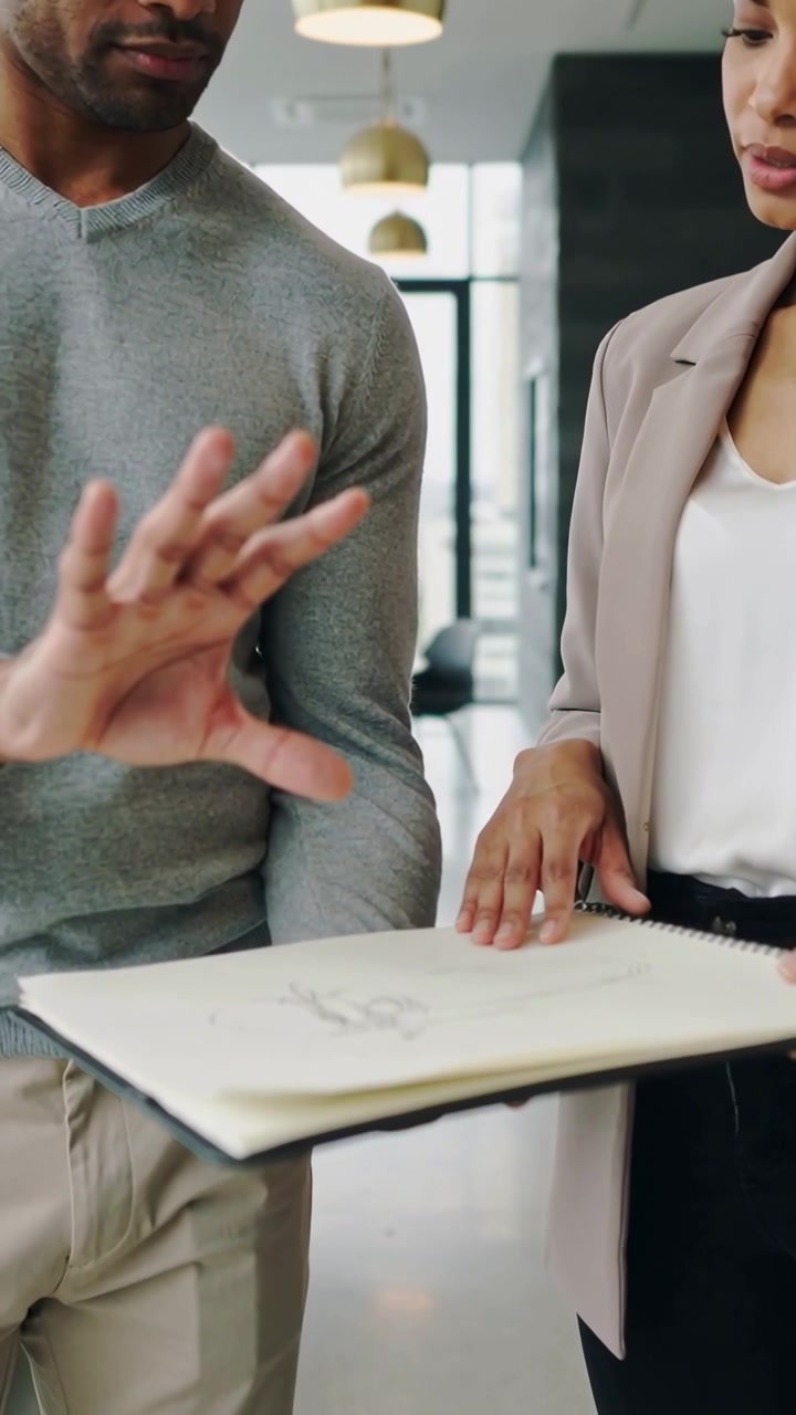 Video verticale: Uomo che indica la dimensione su un quaderno a spirale tenuto da una donna in blazer in ufficio