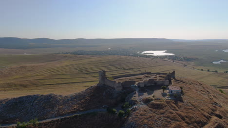 long drone tracking shot of enisala, medieval fortress on top of a hill surrounded by lakes and plains on a clear sunny day