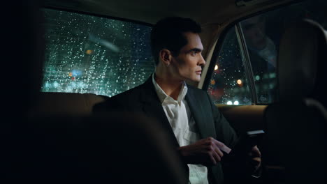 hombre serio desplazando el teléfono en la noche auto de cerca. hombre de negocios trabajando en el coche