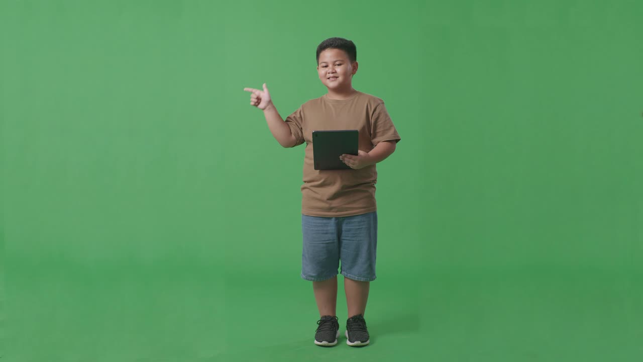 태블릿을 사용하고 스튜디오에서 녹색 화면 배경에 으로 가리키는 아시아 소년의 전체 몸