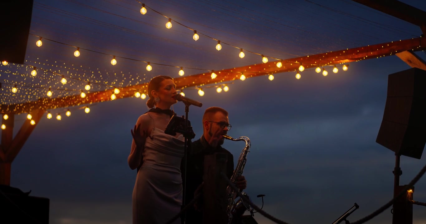 Female Singer and Saxophonist Performing Live on Outdoor Stage at Night
