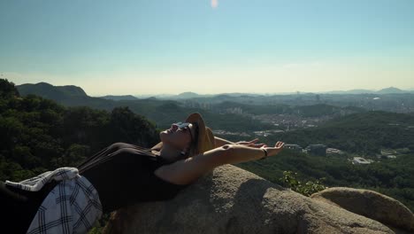 caucasian girl wearing a sunglasses ang looking at the beautiful sky while lying on the rocks at the peak of gwanaksan mountain in seoul, south korea