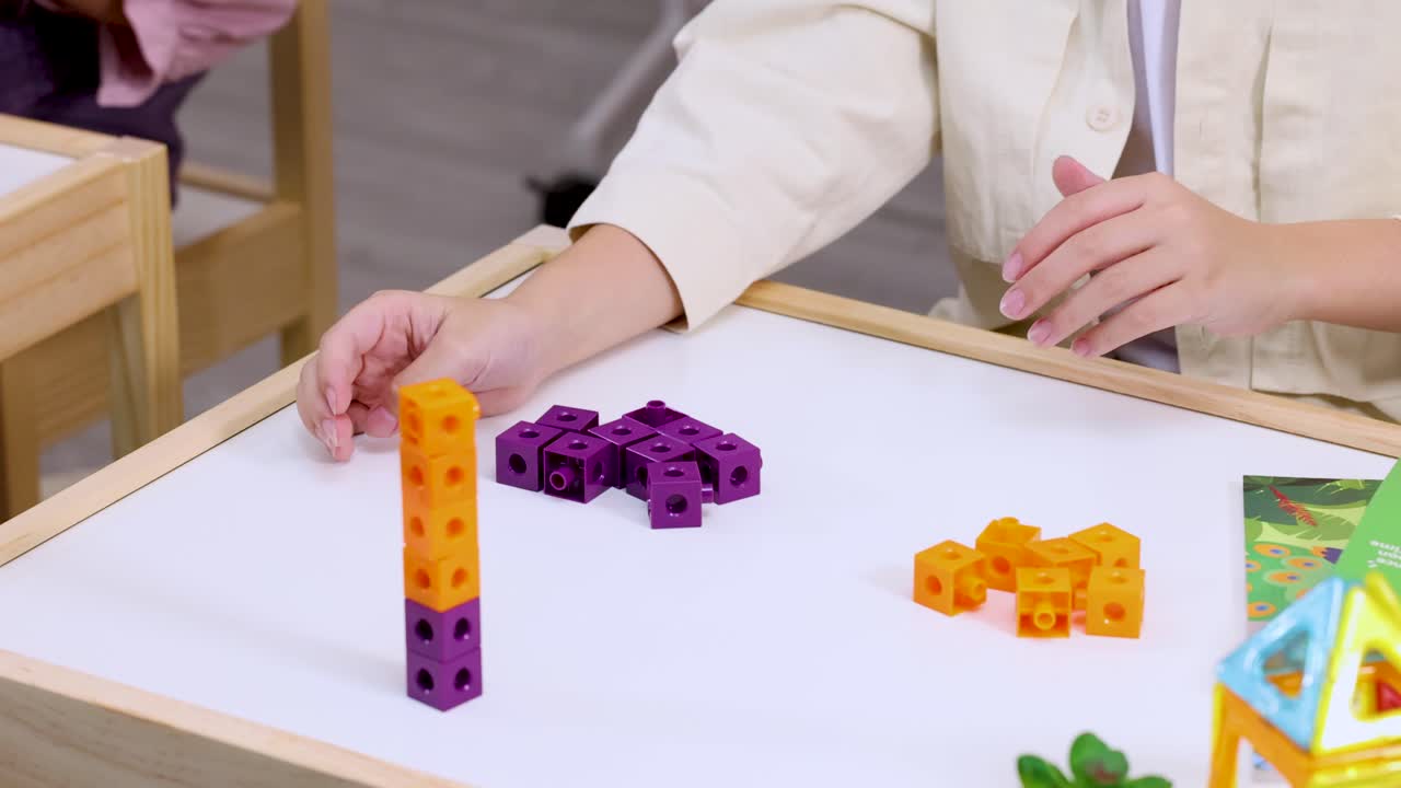 Child carefully stacks interlocking math cubes on white tabletop in bright classroom setting