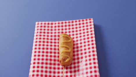 video of corn dog with mustard on a blue surface