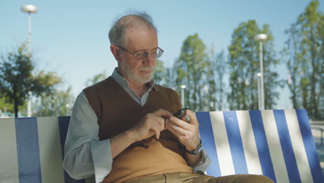 good looking old man sitting on bench outside, texting on phone