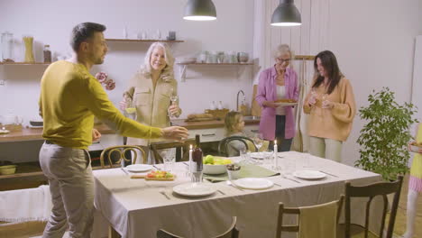 familia feliz, con padres, abuelas y niñas pequeñas, poniendo la mesa juntos y listos para cenar