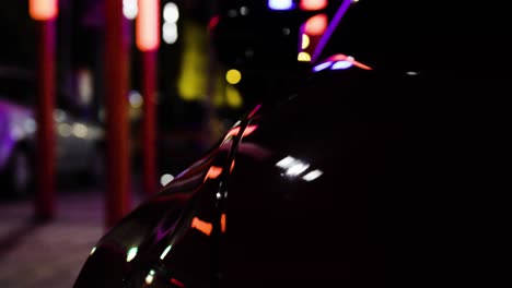 Detail-closeup-rear-carbon-fiber-reflections-in-red-sport-car-in-the-dark-night-in-the-city-standing-static