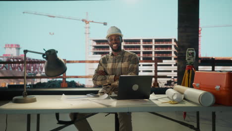 smiling male architect or engineer at a construction site with laptop and blueprints