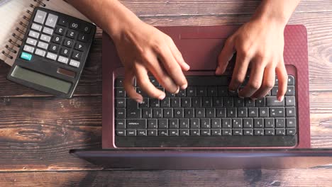 persona que escribe en una computadora portátil con una calculadora y un cuaderno