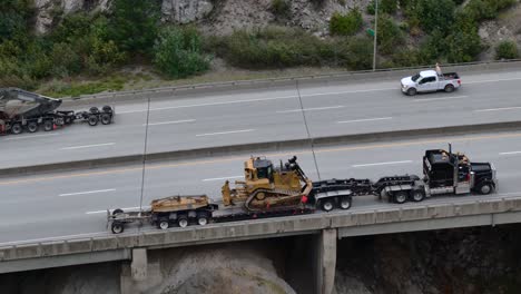 Transporte-De-Carga-Pesada-En-La-Carretera-De-Coquihalla,-Excavadora-Y-Topadora-Se-Mueven-En-Una-Pendiente-Pronunciada