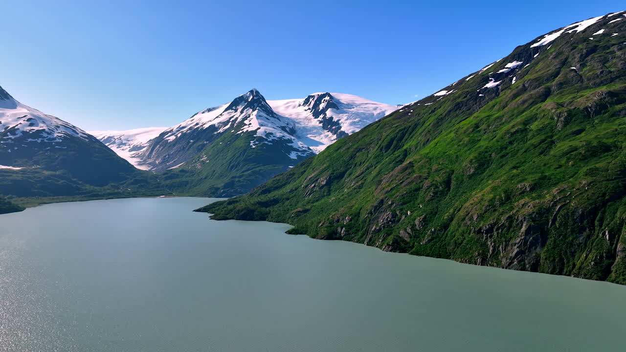 Breath-taking scenery of mountains covered with some snow. A wide peaceful river is at the rocks foot. Alaska, USA. Aerial view