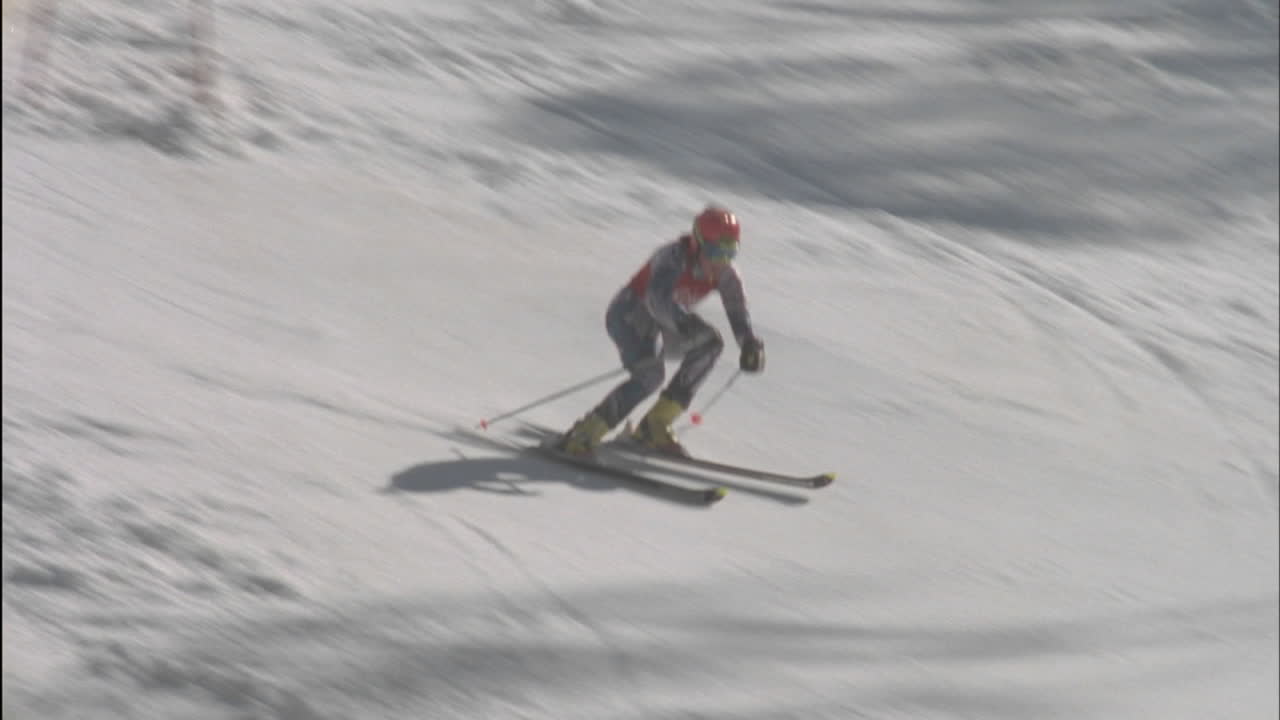 한 스키어가 언덕 아래로 스키를 타고 바닥에 있는 깃발을 치고 있다