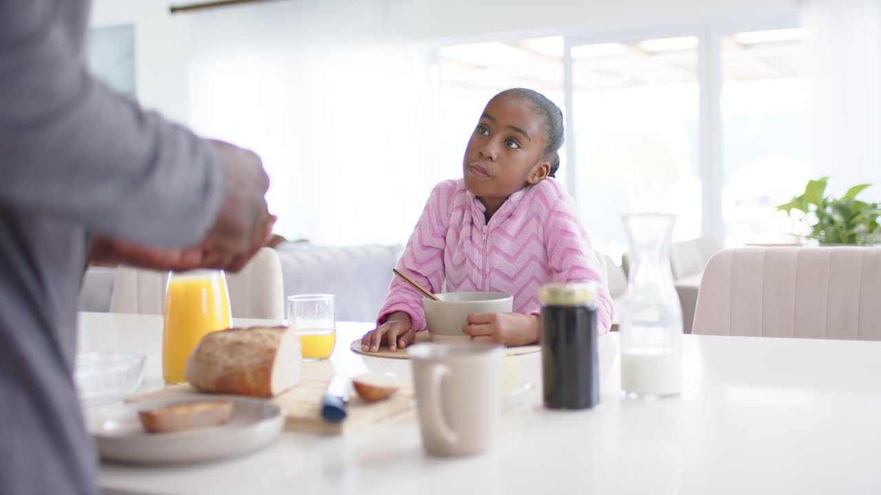 African American father picking bread showing toast as child holding bowl spoon at kitchen counter