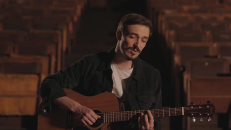un bel ragazzo suona una chitarra acustica in un cinema abbandonato. il musicista canta una canzone e accompagna con la chitarra