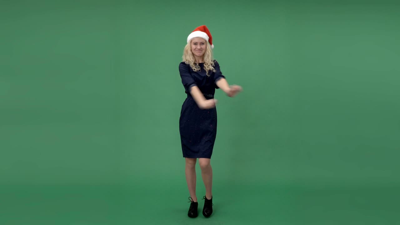 산타의 모자를 입은 젊은 금발 여성이 춤추고 놀고, 크로마 키 녹색 화면