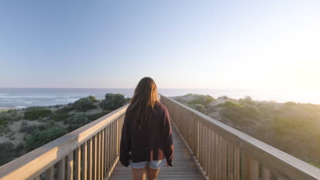 follow shot of young girl smiling and walking along jetty at beach during sunset