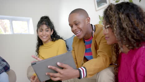 Happy-diverse-group-of-teenage-friends-using-tablet-and-talking-at-home,-slow-motion