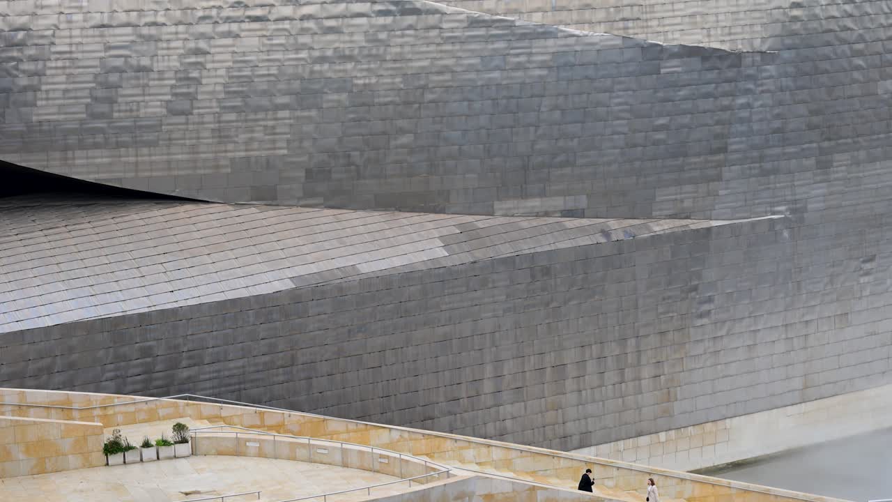 Visitors make their way down the stairs at the Guggenheim Bilbao, with Frank Gehry’s striking steel facade blending light and sky, a standout example of deconstructivism in Bilbao, Spain.