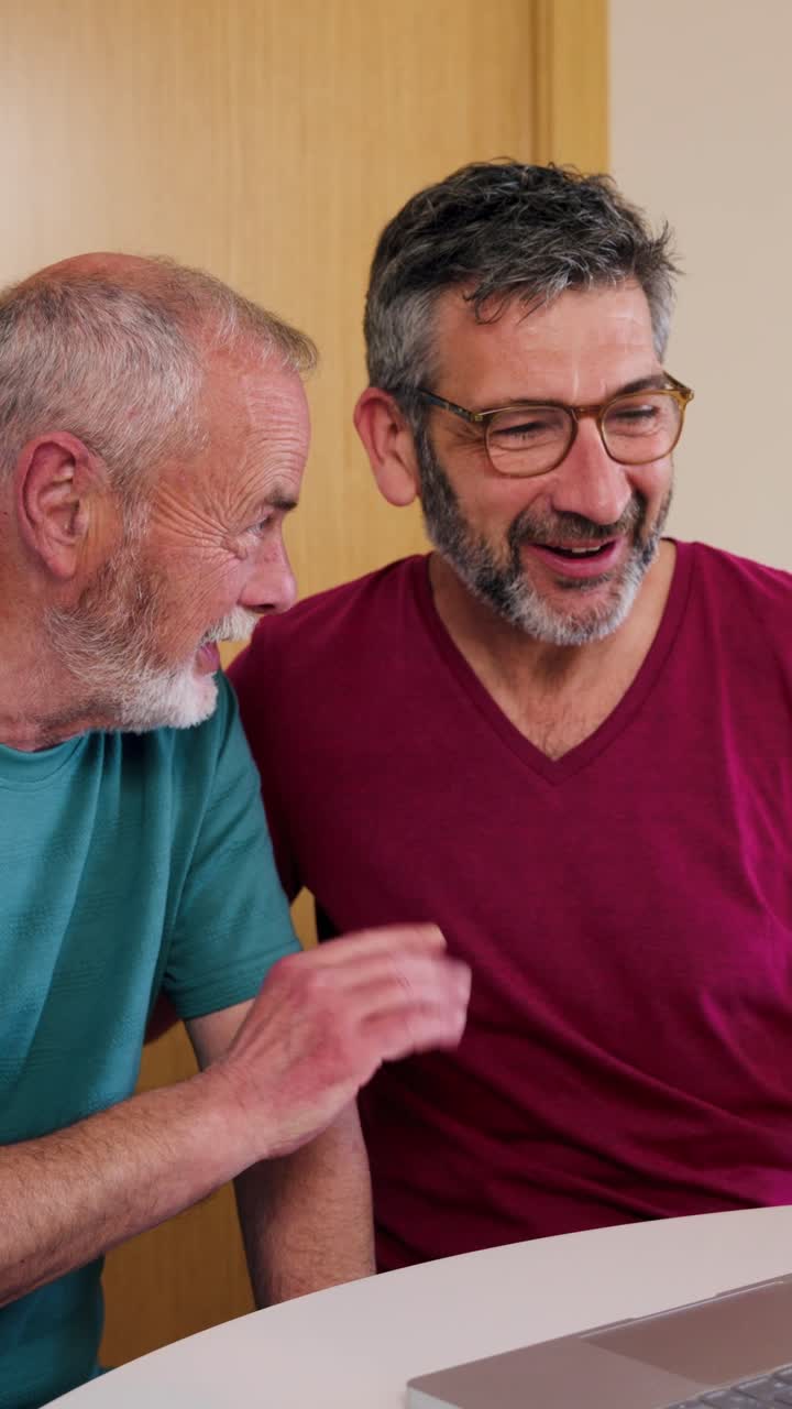 Dos hombres felices riendo y hablando mientras miran un portátil