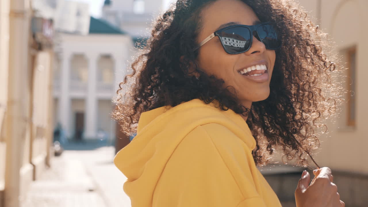 mujer sonriente con capucha amarilla y gafas de sol afuera