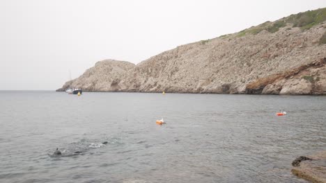snorkeller swimming in calm waters near rocky cliffs at cala morell, menorca, spain