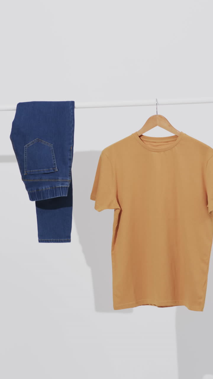 Vertical video of denim jeans and yellow t shirt on hanger and copy space on white background