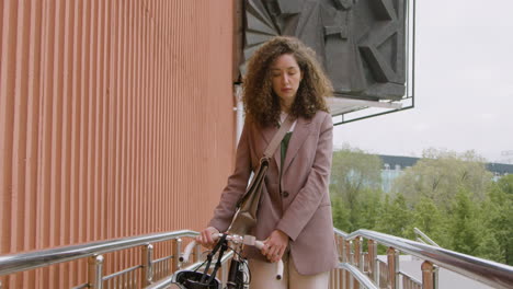 pretty curly woman in formal clothes walking to the office with her bike