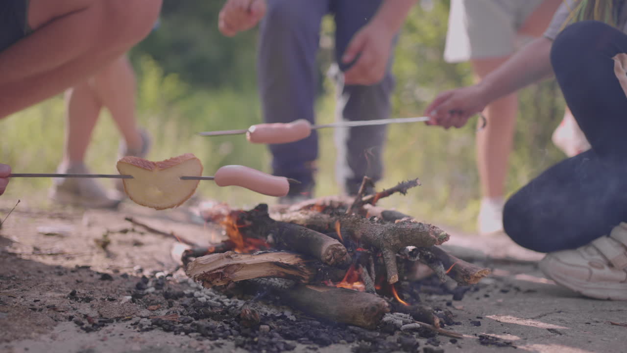 дети в летнем лагере жареют колбасу на костре.