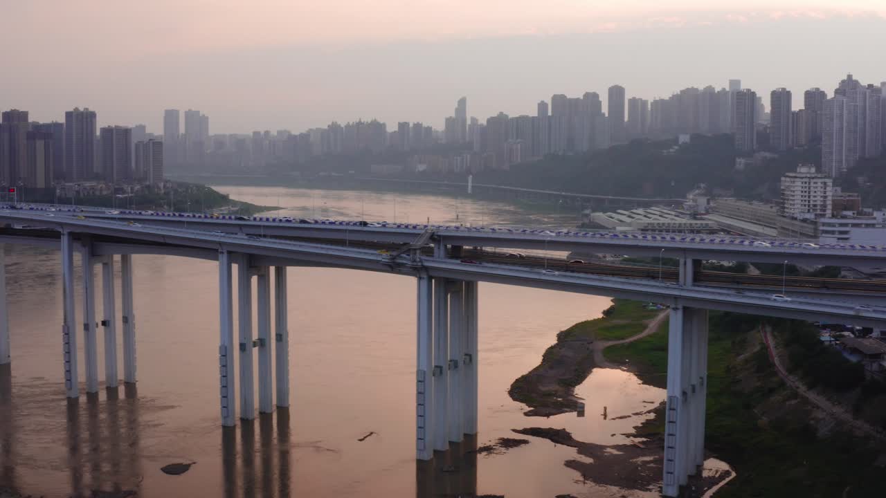 Busy highway bridge crosses river with Chongqing city china hazey skyline, aerial trucking pan