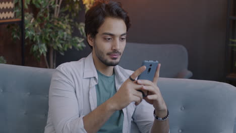 man laughing at his phone on a couch