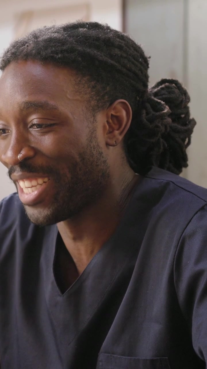 Vertical video: Camera revealing man in scrubs talking, laughing to listener at table with plant