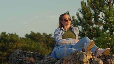 Young-woman-sitting-on-rocks,-nature,-sunset