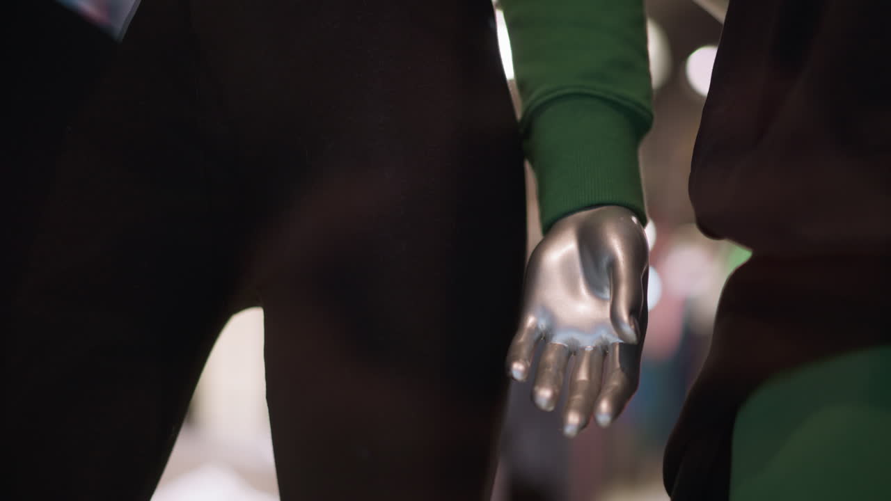 Close-up view of a silver mannequin hand with dressed in in black trousers and green sleeve, against a blur background