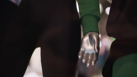 close-up view of a silver mannequin hand with dressed in in black trousers and green sleeve, against a blur background