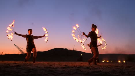 professional artists show a fire show at a summer festival on the sand in slow motion. fourth person acrobats from circus work with fire at night on the beach.