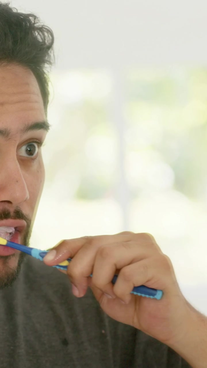 Vertical video: Bringing brush, man in grey tee brushing teeth at vanity for hygiene, copy space