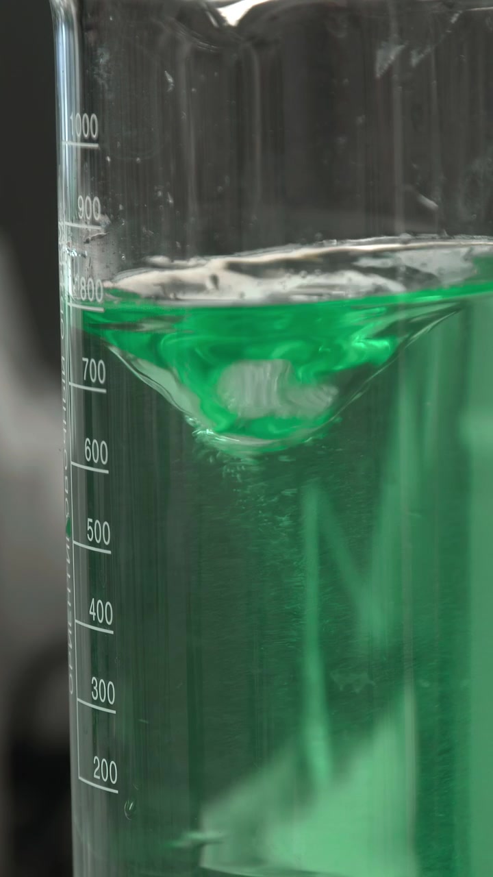 Beaker With Green Vortex Stirring Liquid In Closeup On Magnetic Stir Plate, Transparent Glass Marked