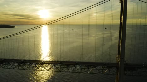 aerial, traffic on large suspension bridge with sunset over ocean in background