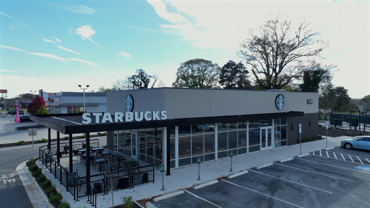 Starbucks Store in suburb of american town during sunny day. Autumnal day with colored trees in rural area. Aerial rising drone wide shot.