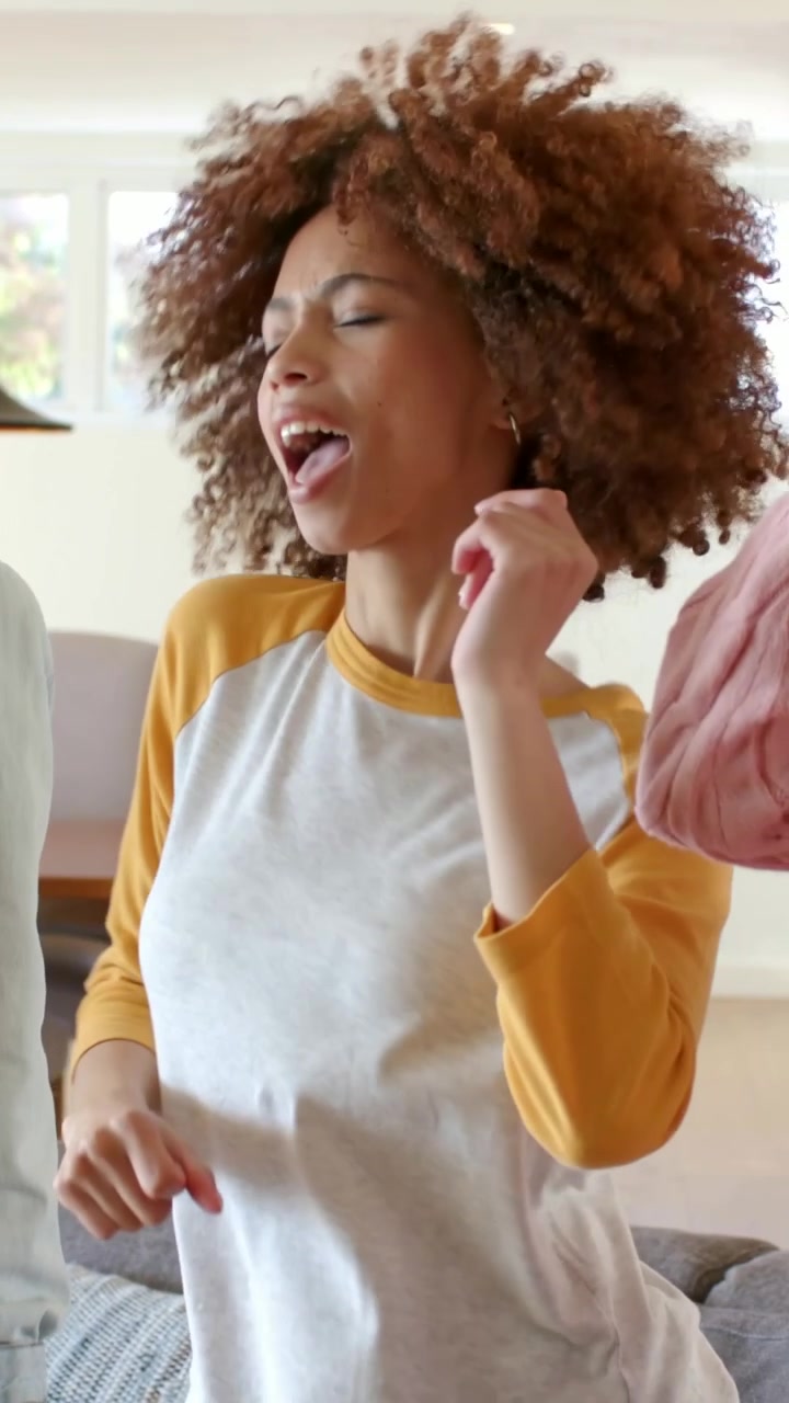 Video verticale: La musica inizia, una donna con gli occhiali canta con gli amici a casa, indossando jeans.