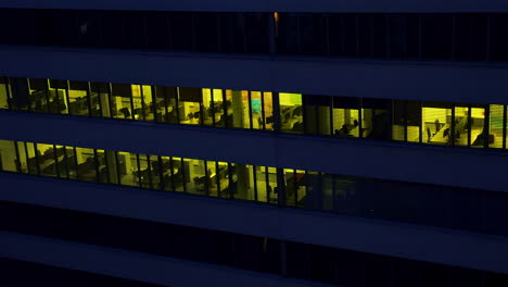 multi-storied office building with desks and tables. dark time footage outside the building with light switched on inside