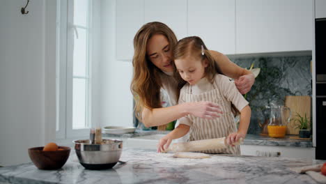 Madre-Cariñosa-Enrollando-Mangas-A-Su-Hija-En-El-Primer-Plano-De-La-Cocina.-Niño-Ayudando-A-Sus-Padres