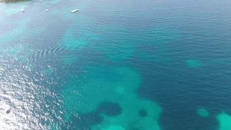 Drone-view-in-Albania-flying-over-blue-crystal-clear-water-and-a-green-small-island,-sunny-day-in-Ksamil